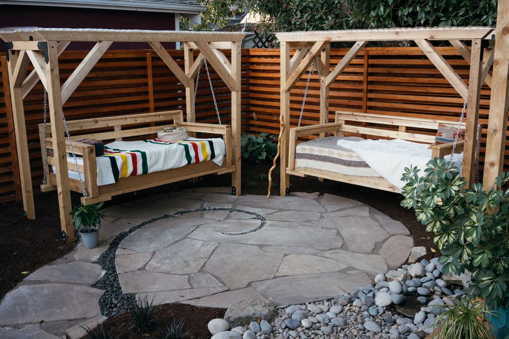 Cozy outdoor swings with cushions nestled in a stone patio garden setting.