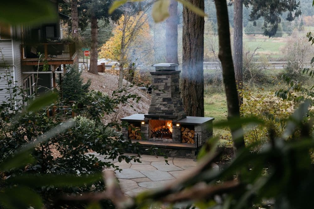 Stone outdoor fireplace surrounded by greenery, creating a cozy ambiance in nature.