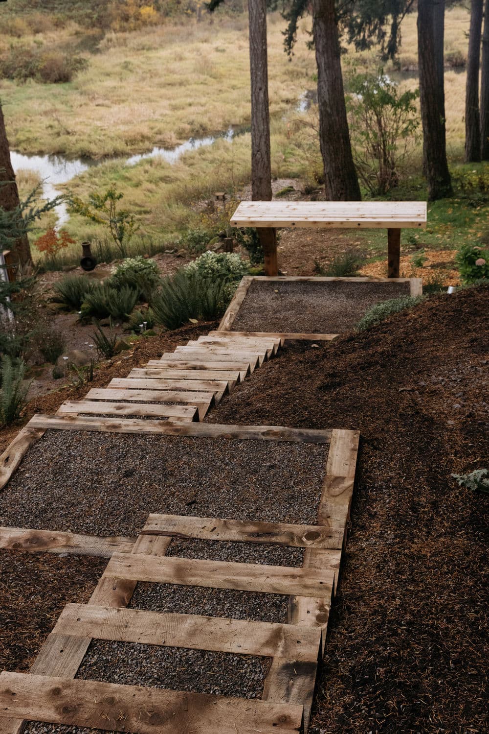 Wooden stairs lead down to a serene river view surrounded by greenery and trees.